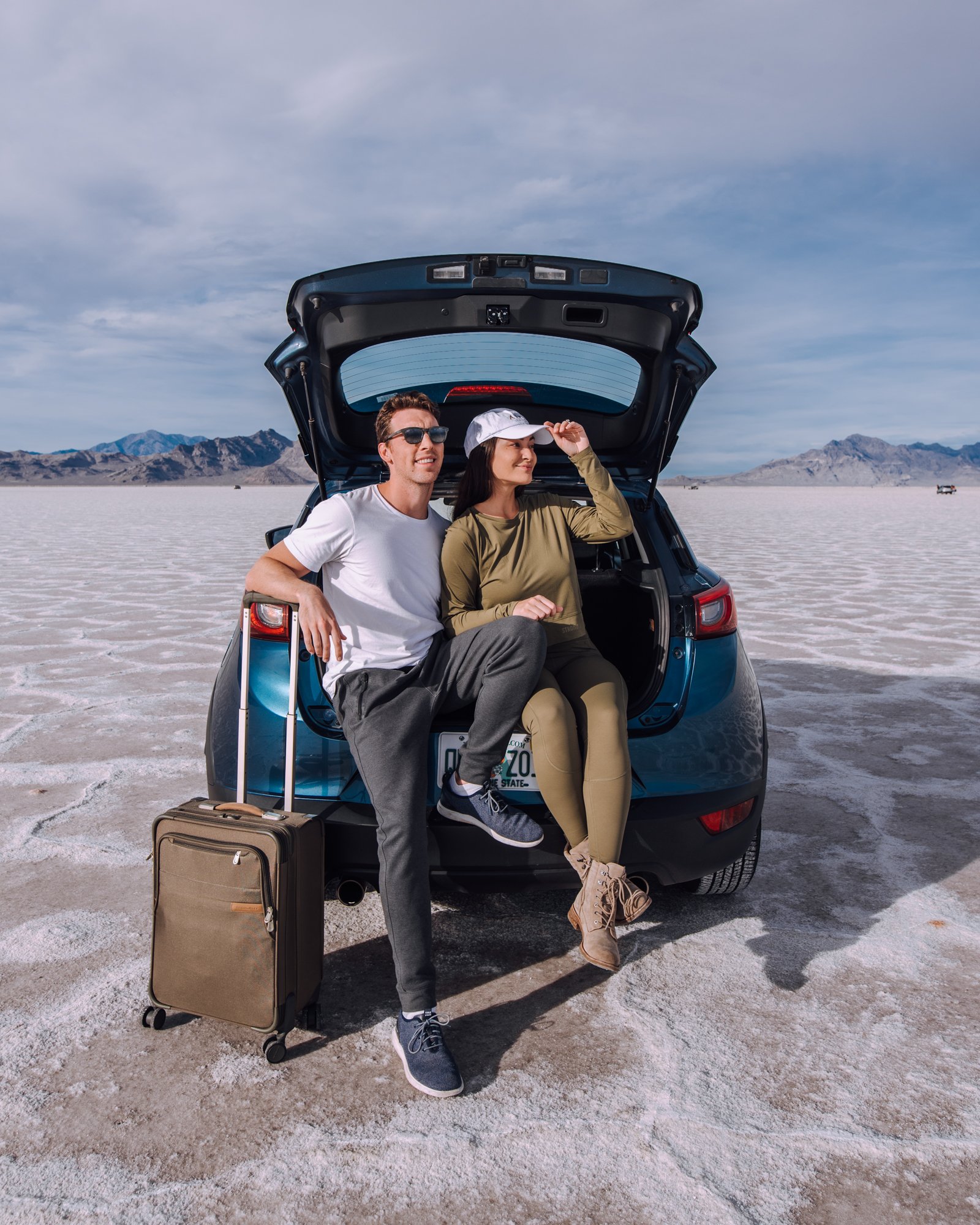 Couple sitting with a suitcase in the open trunk of a car on the Bonneville Salt Flats in Utah.