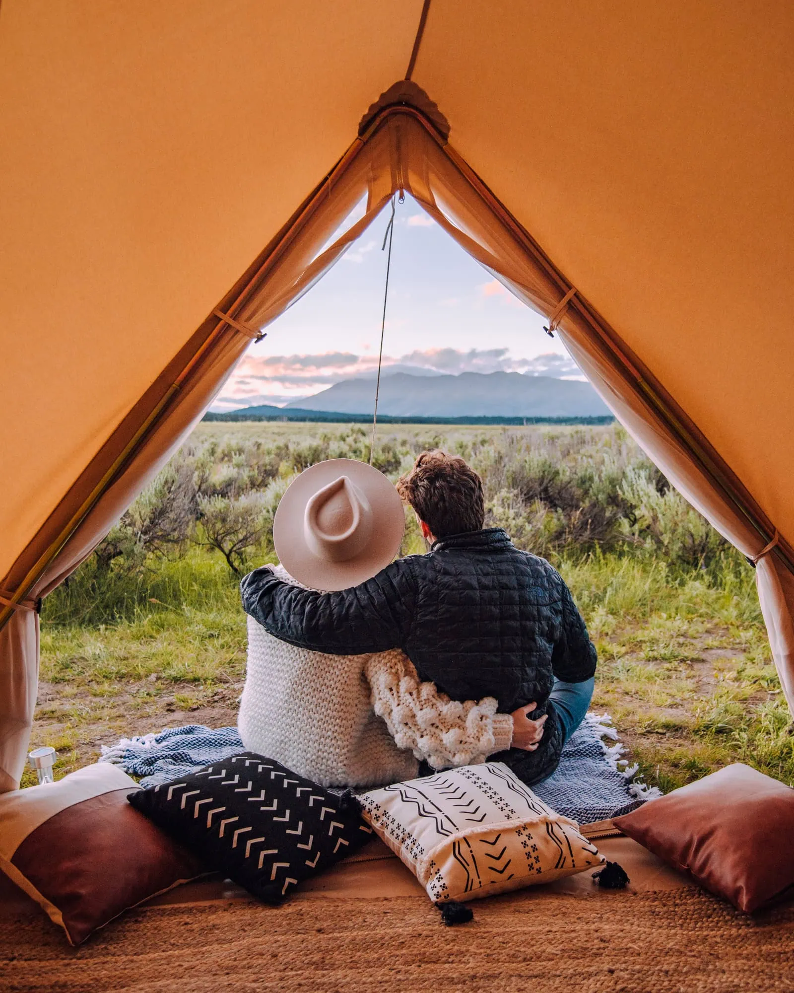 The view looking outside of a tent with a couple sitting and looking out at the mountains outside of Yellowstone in Idaho.