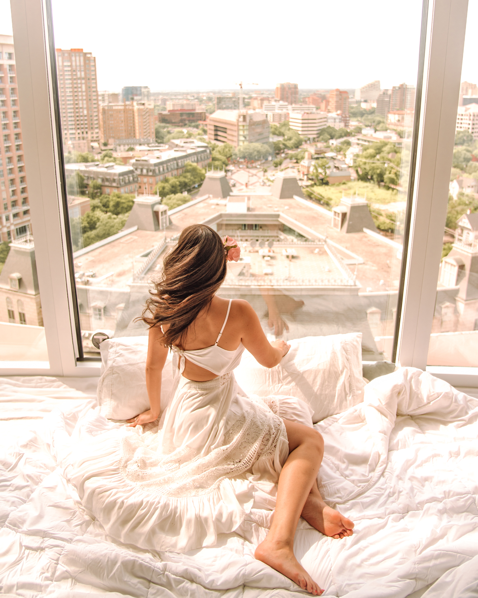 girl on a bed in front of a giant window with a view.