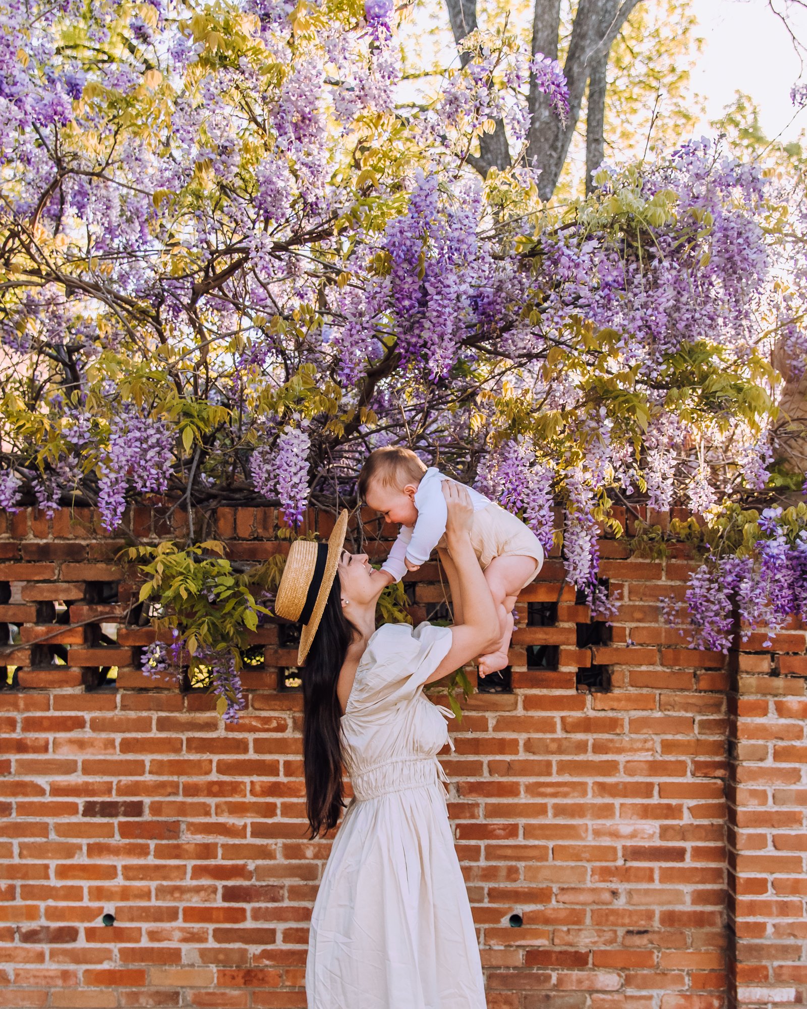 Mom and baby posing in front of wisteria wall