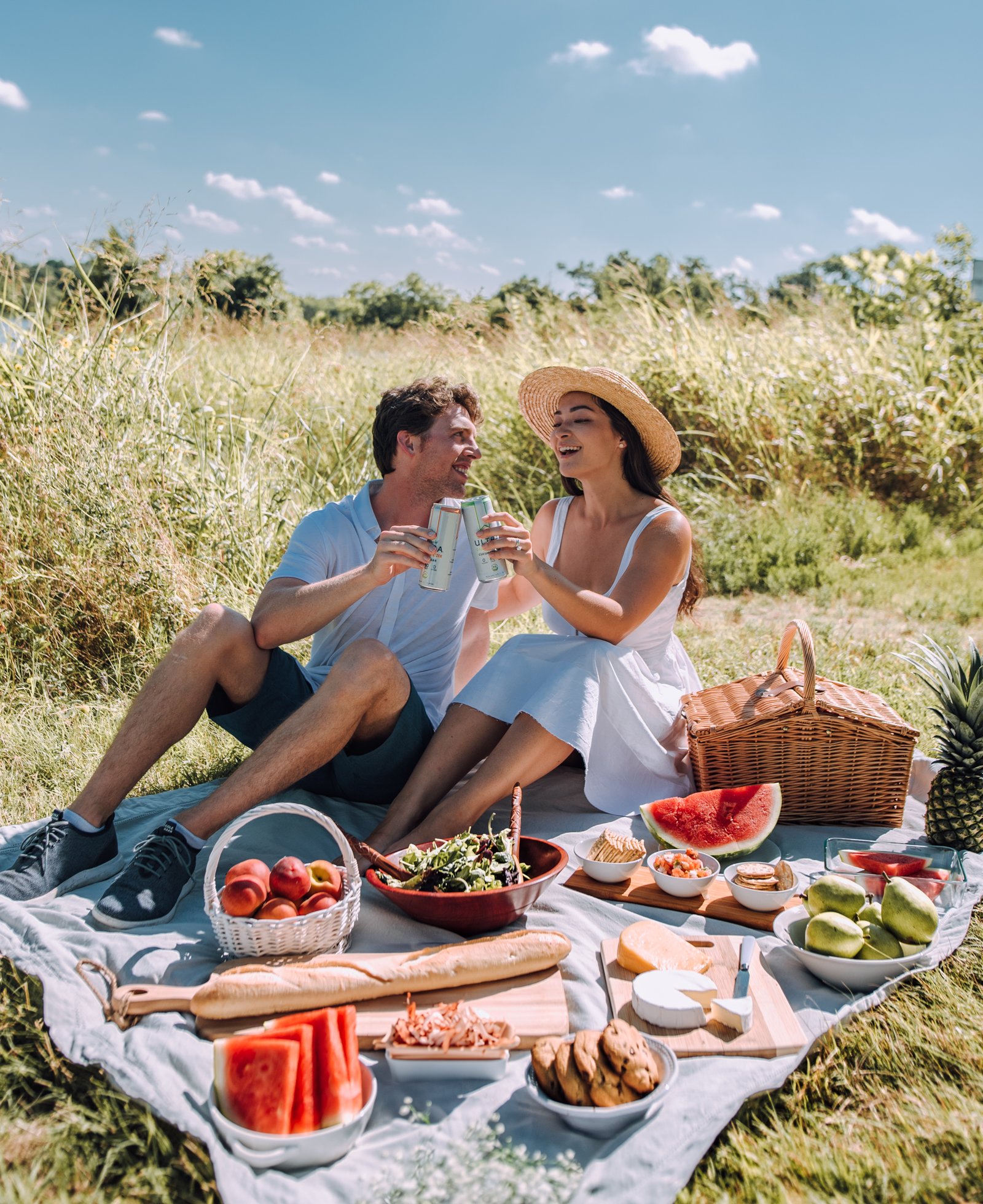 A couple doing a cheers at a romantic picnic in a field.