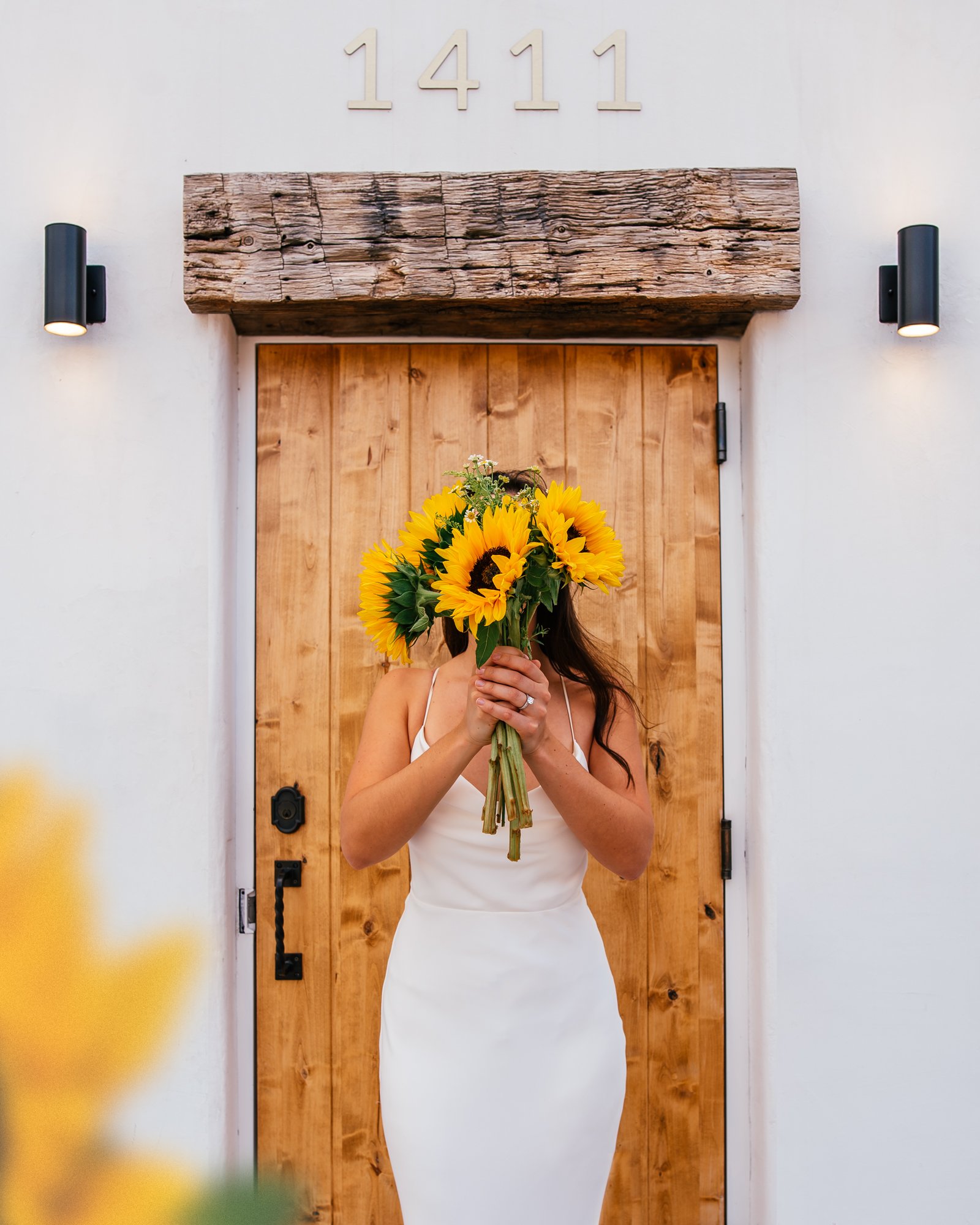 Girl wearing a white wedding dress while holding sunflowers in front of her face