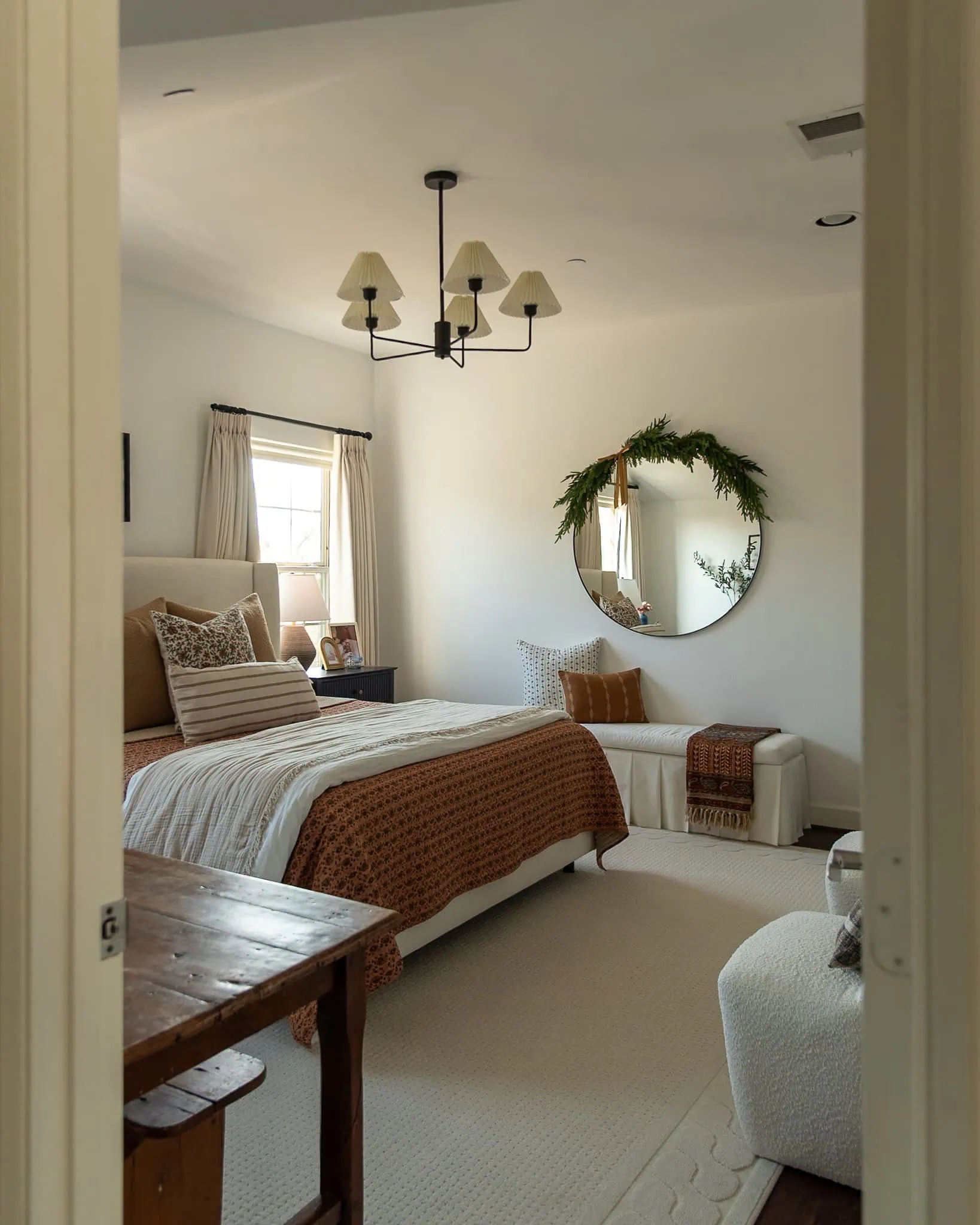 Realistic faux cedar garland draped asymmetrically over a round bedroom mirror with a velvet ribbon tie